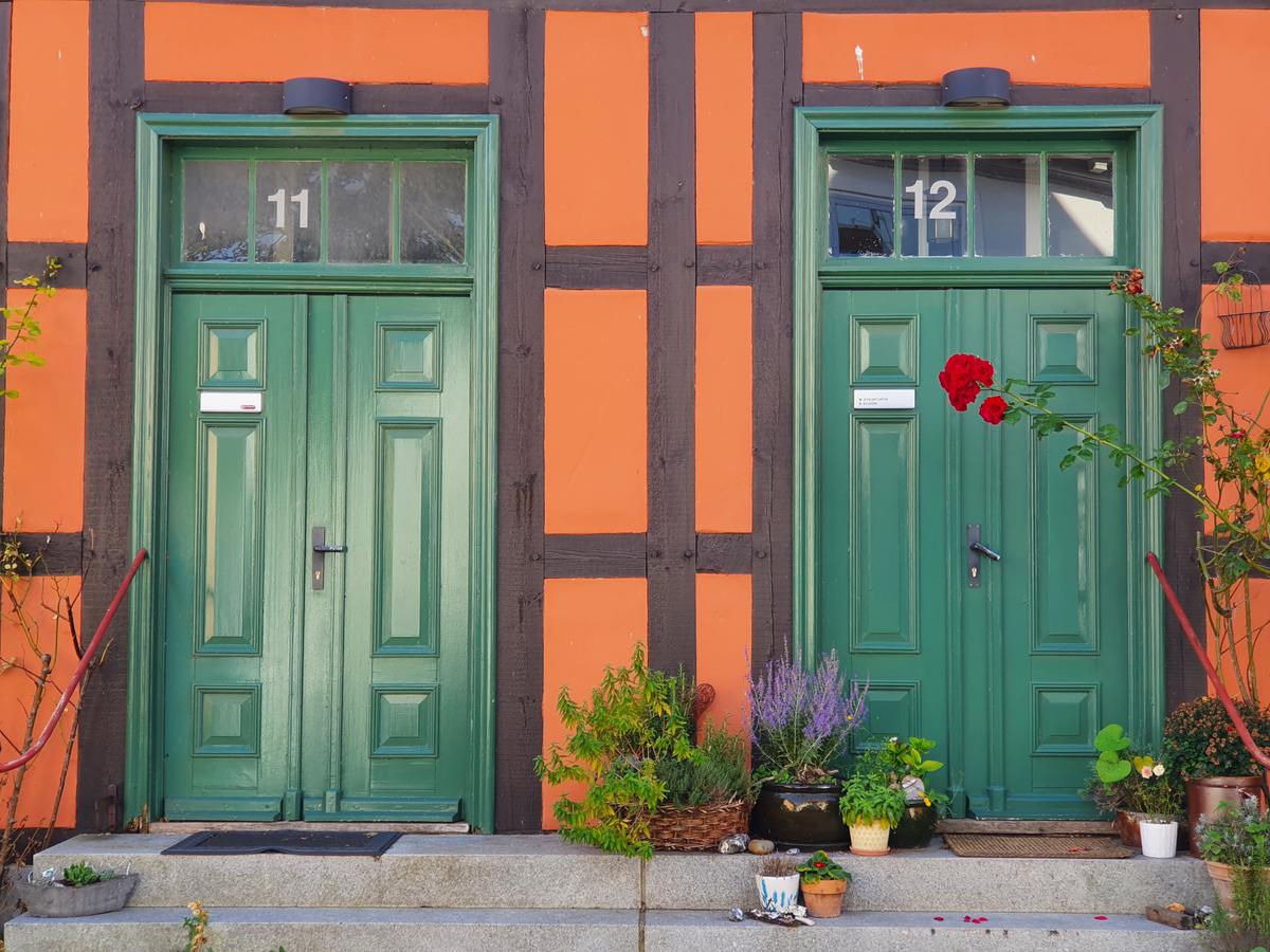 rote Hauswand Fachwerkhaus grüne Holztüren Blumen im Vordergrund