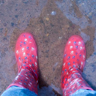 Rote Gummistiefel von oben fotografiert in einer Pfütze